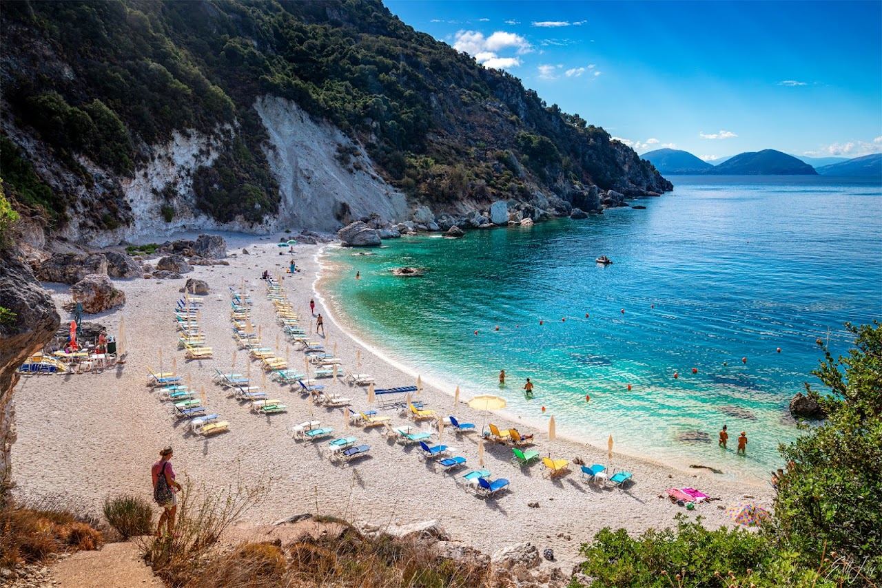 A small cove of white pebbles and clear turquoise water framed by green hills at Agiofili beach near Vasiliki in southern Lefkada