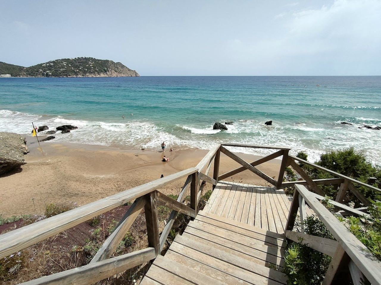 Tall clay coloured cliffs rising behind the dark sand and clear water of Aguas Blancas on the northeast coast of Ibiza
