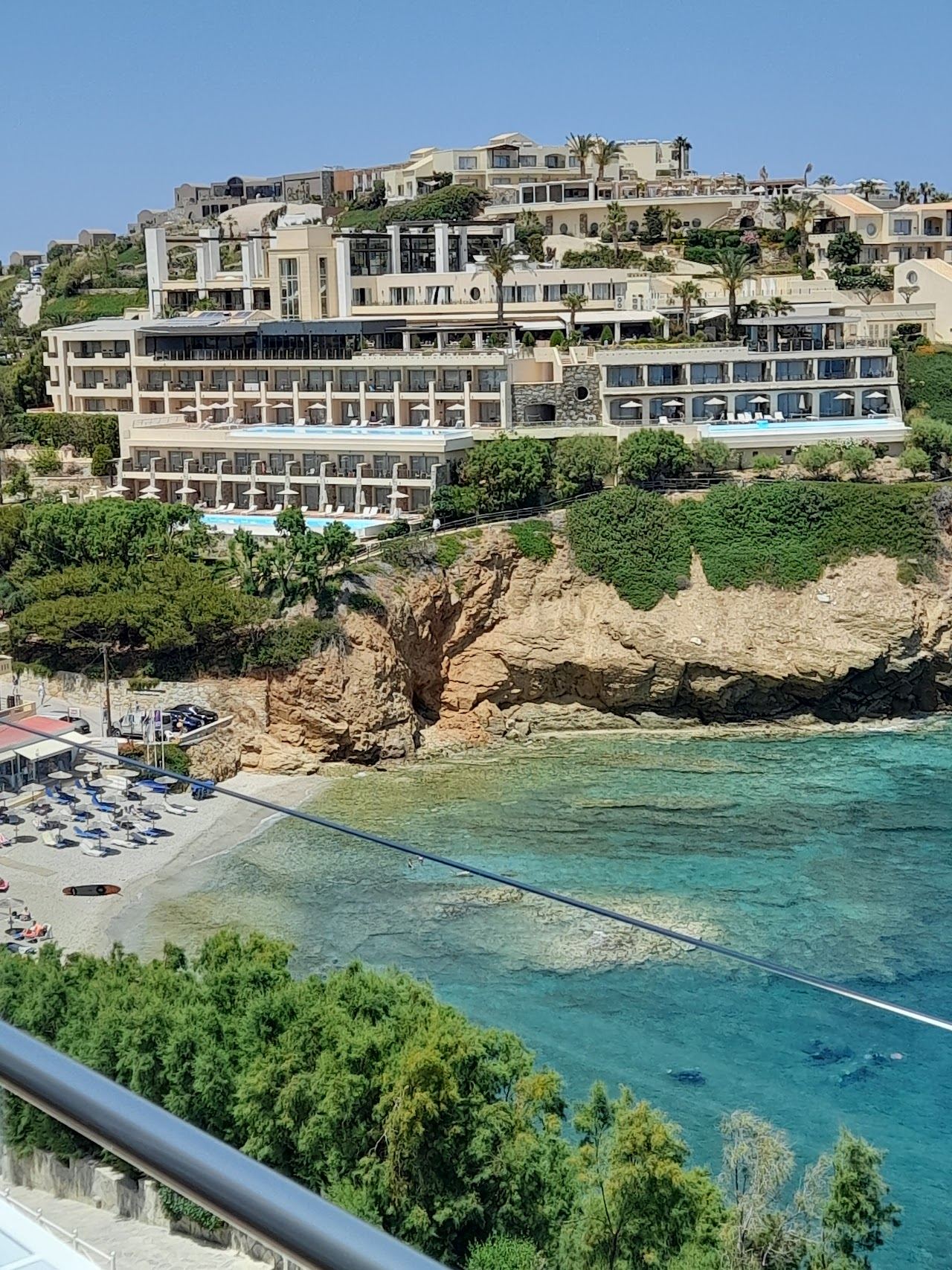 Hotel terraces stacked on the headland above a small clear water cove beside Agia Pelagia