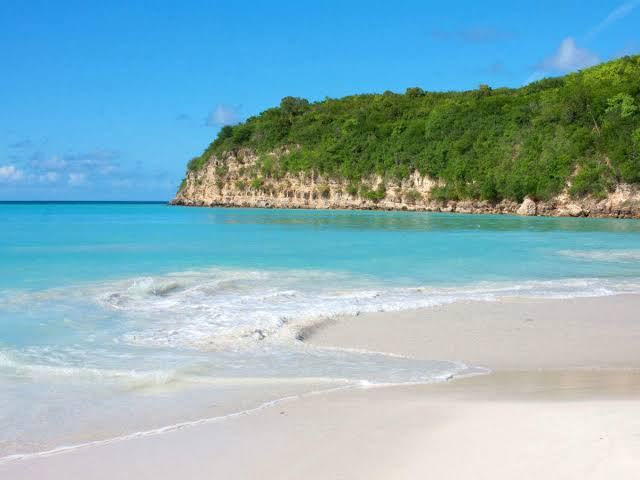 Calm turquoise water and soft white sand along the resort lined sweep of Dickenson Bay in Antigua