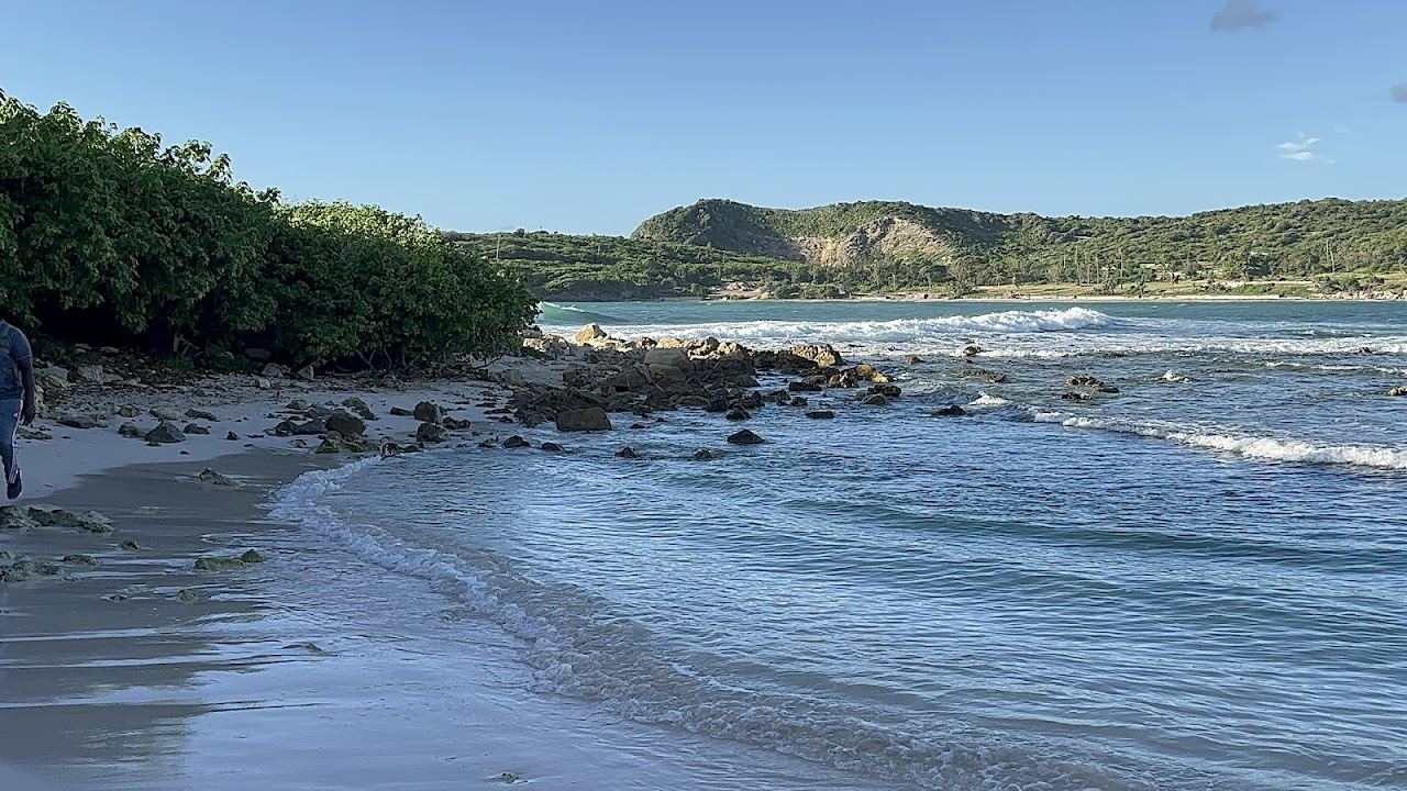 Green headlands framing the pink sand crescent and blue Atlantic water of Half Moon Bay in Antigua