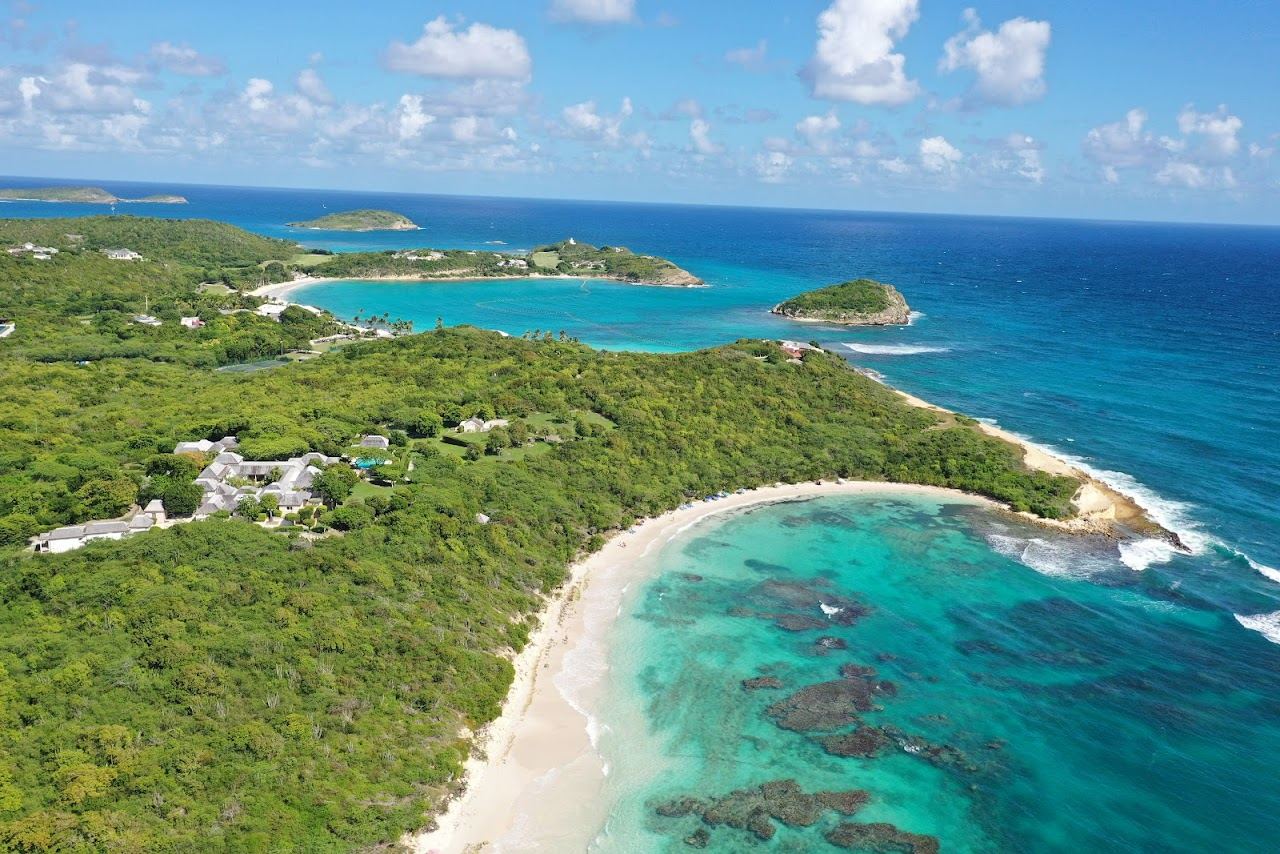 Pink tinged sand and white capped blue water on the wide Atlantic crescent of Half Moon Bay in Antigua