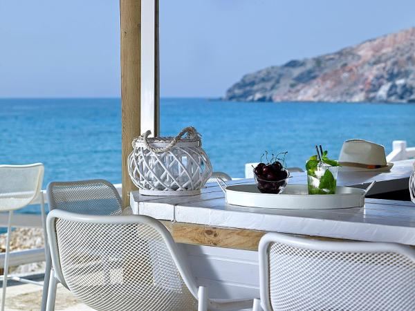 Sunbeds and straw umbrellas of the Aqua Loca beach bar by the water on Paliochori beach in Milos