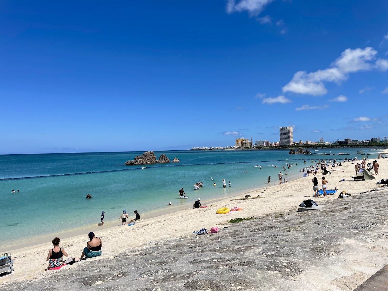 The white sand and blue water of Araha Beach in Chatan, Okinawa, with the promenade and park behind