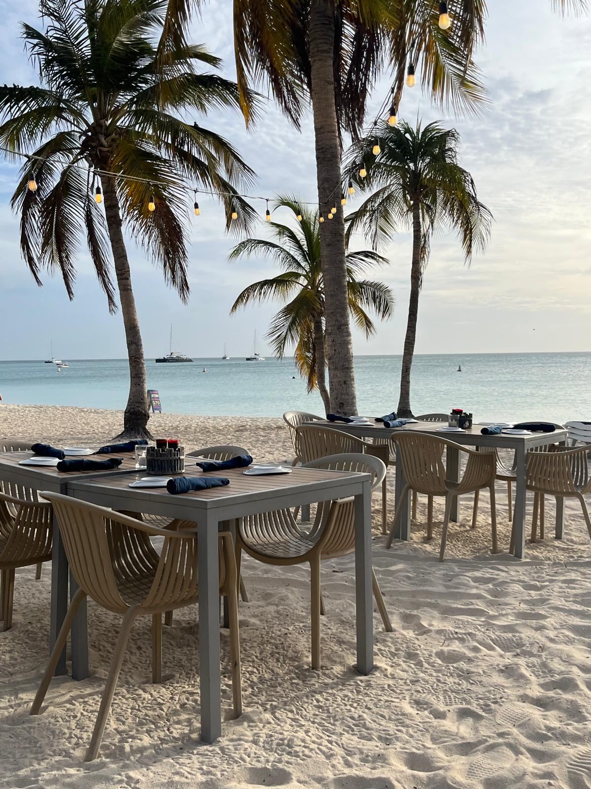 Beach bar loungers and palm shade on the Palm Beach sand at sunset in Aruba