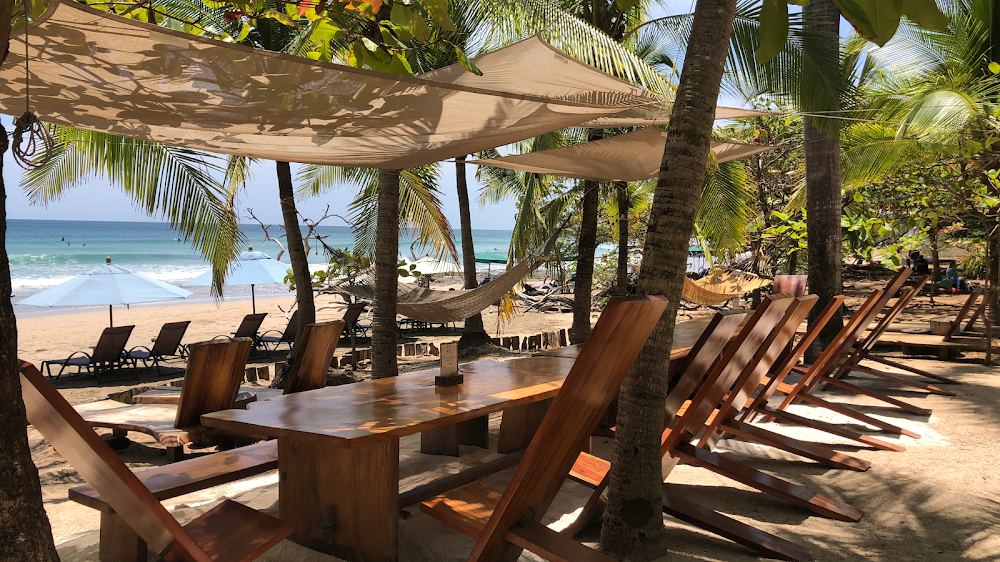 Shaded wooden tables and loungers facing the surf at Lola's on Playa Avellanas
