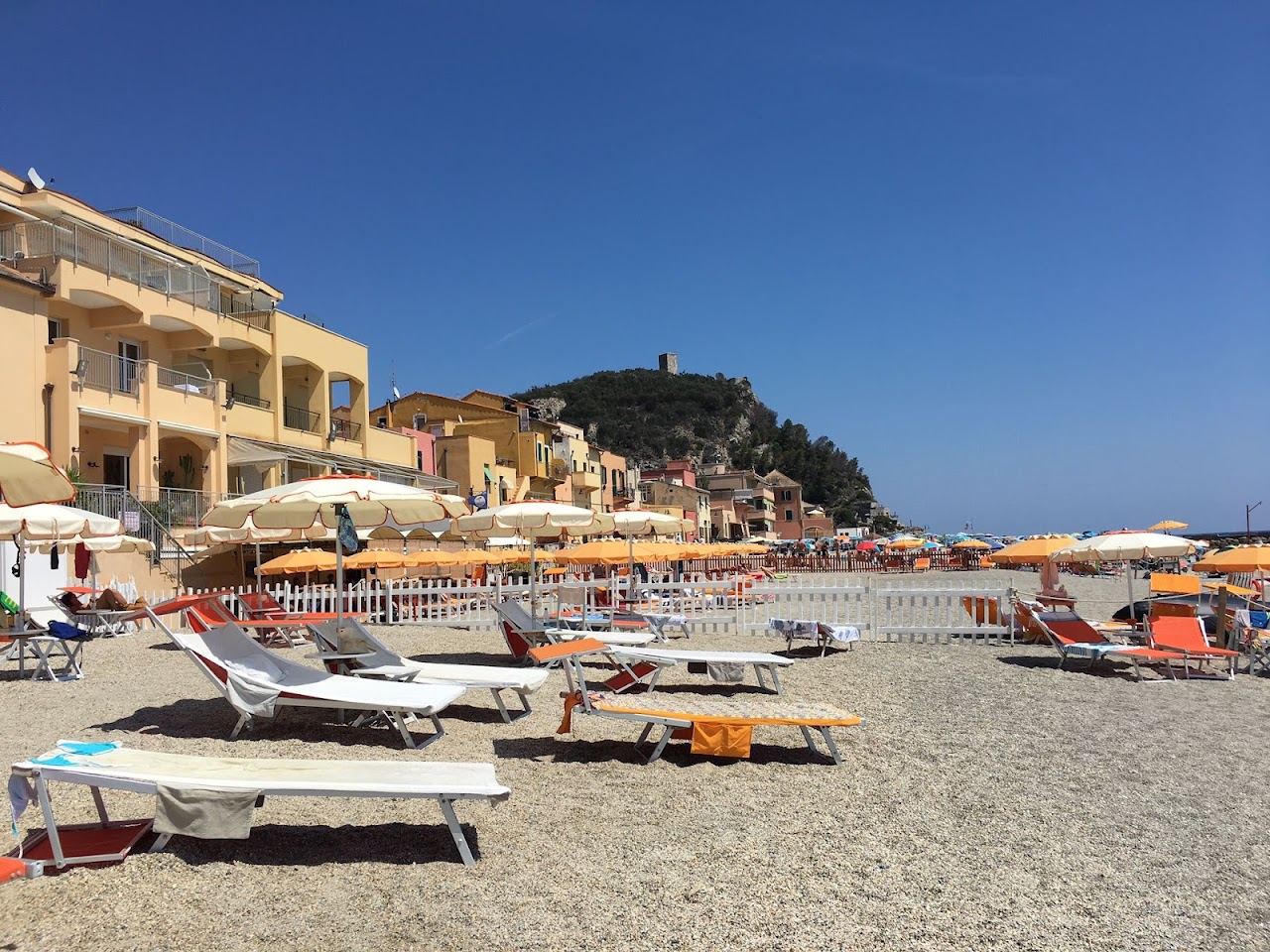 Umbrellas and loungers of Bagni La Giara on the sand of Varigotti with the pastel houses of the old village behind