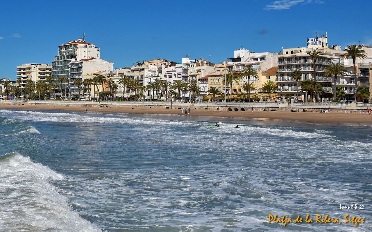 Golden sand, calm water and the white town backdrop of Platja de la Ribera in Sitges