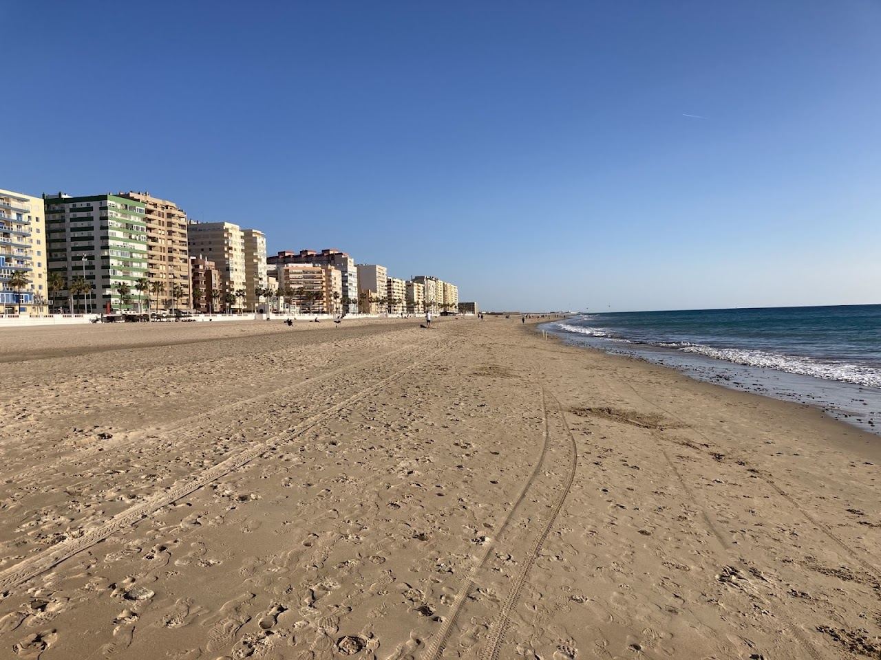 A long wide Atlantic city beach of pale sand and blue water at Playa de la Victoria in Cadiz, Spain