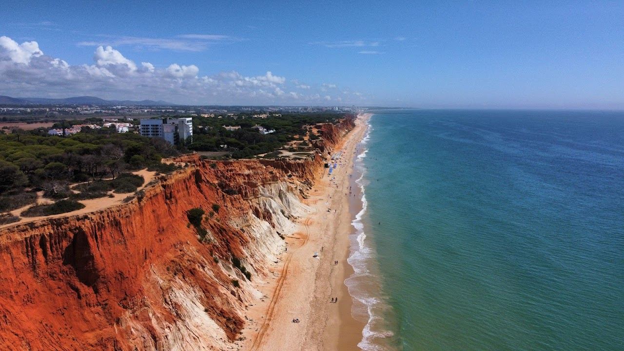 Rust and ochre cliffs above a long ribbon of pale sand and blue sea at Praia da Falesia in the Algarve