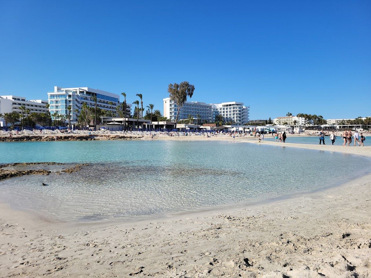 Bright white sand and luminous turquoise shallows with a small islet at Nissi Beach in Ayia Napa, Cyprus