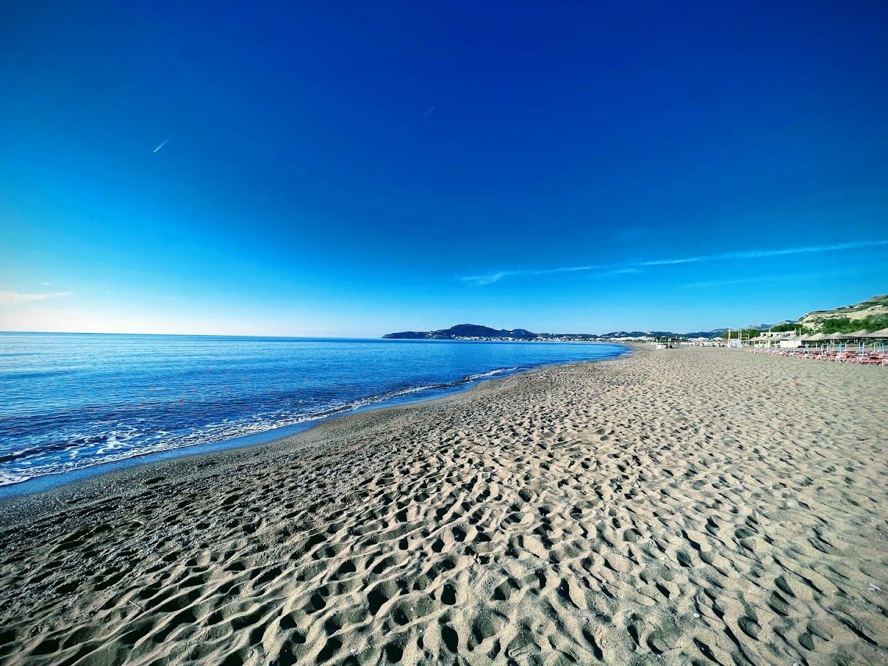 A long curve of golden sand and calm blue water with sunbeds at Faliraki beach on Rhodes, Greece