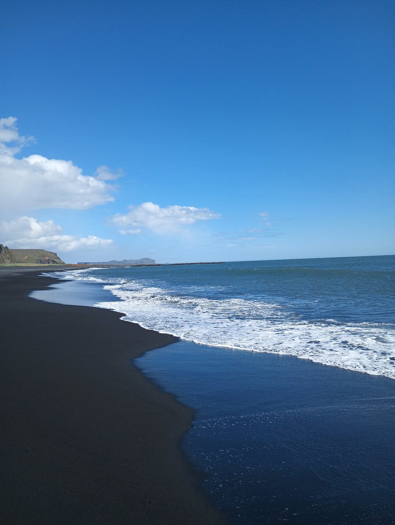 Dark volcanic sand and basalt columns meeting white surf on a dramatic black beach