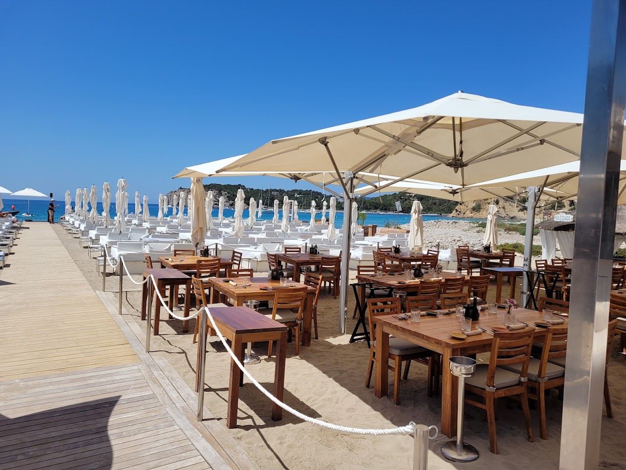 Large white day beds and parasols on the pebble cove in front of Blue Marlin Ibiza at Cala Jondal