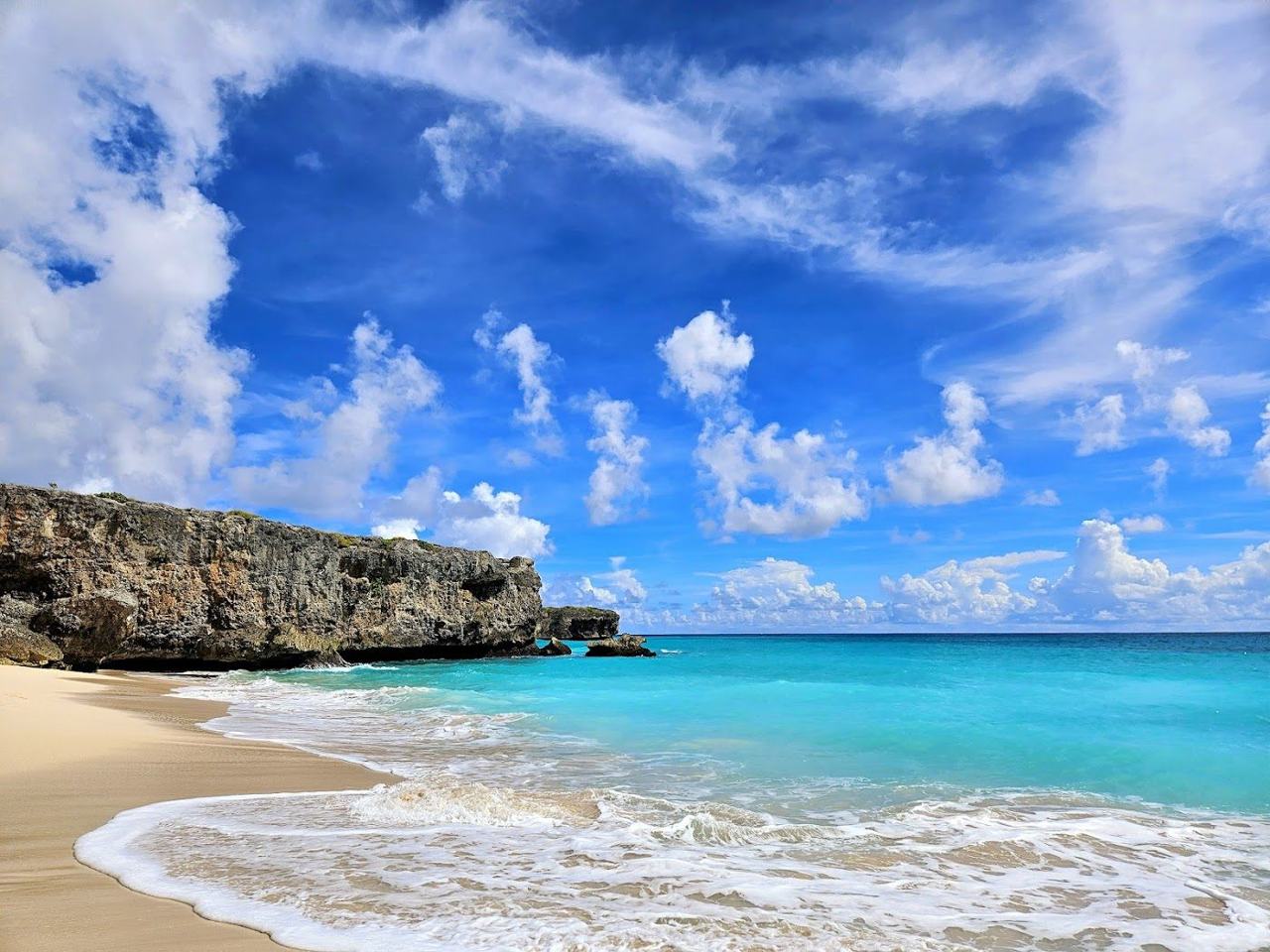 Coconut palms, cliffs and Atlantic surf framing the white sand of Bottom Bay in south east Barbados