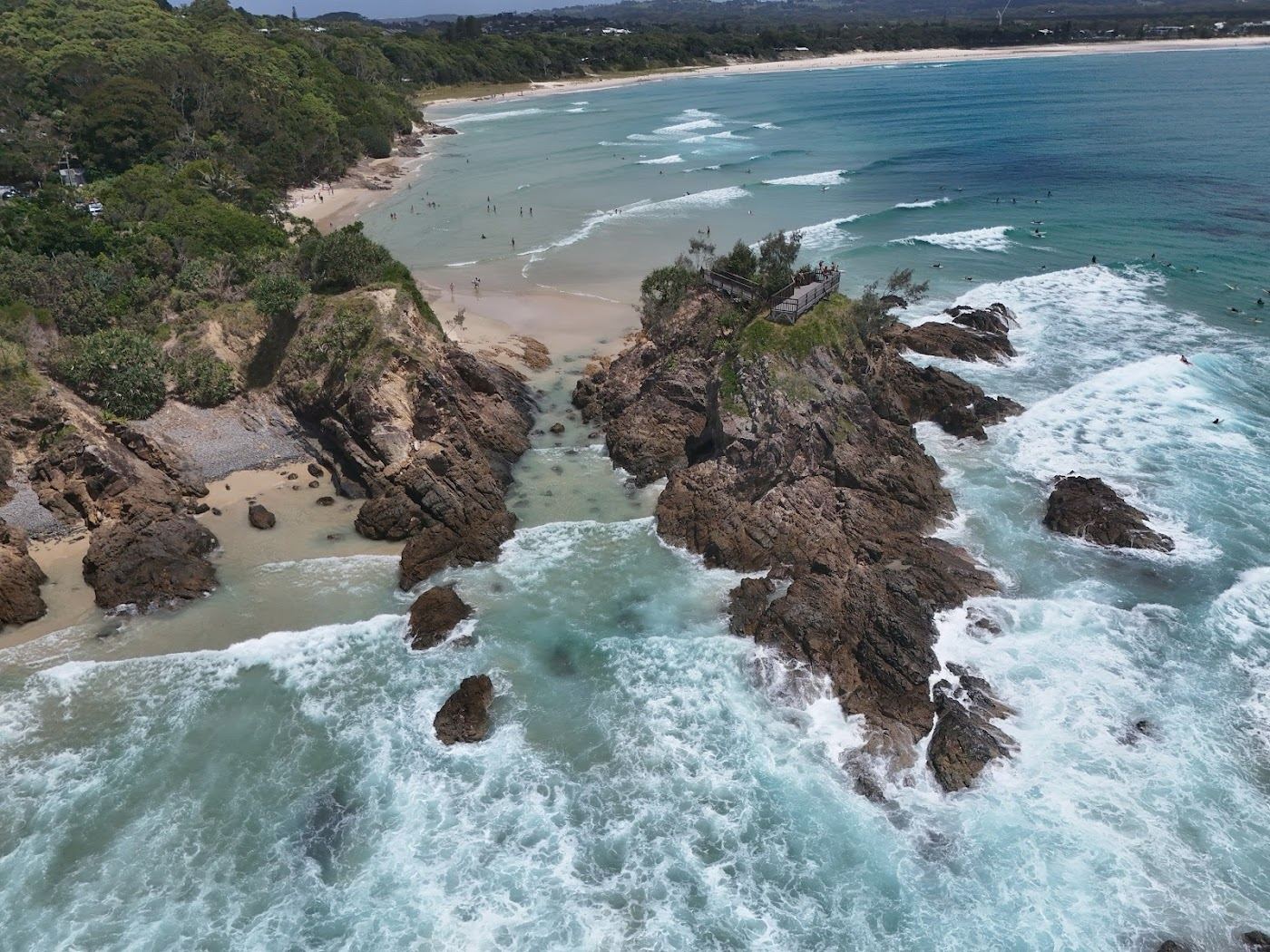 Surfers in the water at The Pass point break beneath the Cape Byron headland in Byron Bay