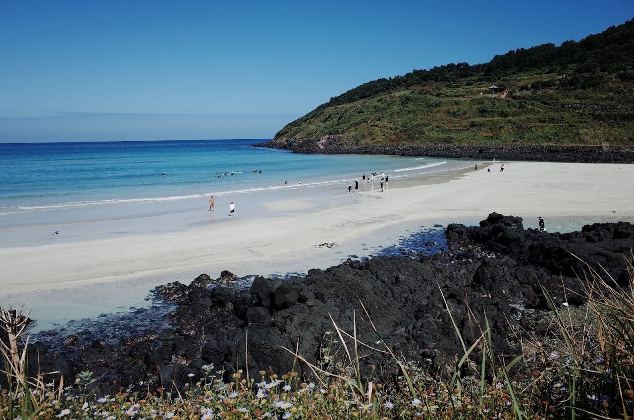 White sand and shallow emerald water at Hamdeok Beach with Seoubong hill behind in Jeju
