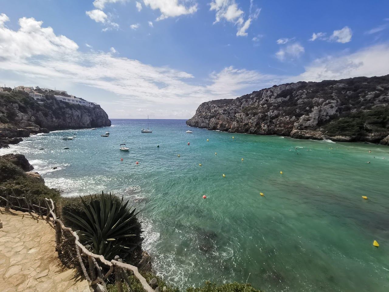 Wide sandy cove enclosed by high cliffs with calm water at Cala en Porter in Menorca