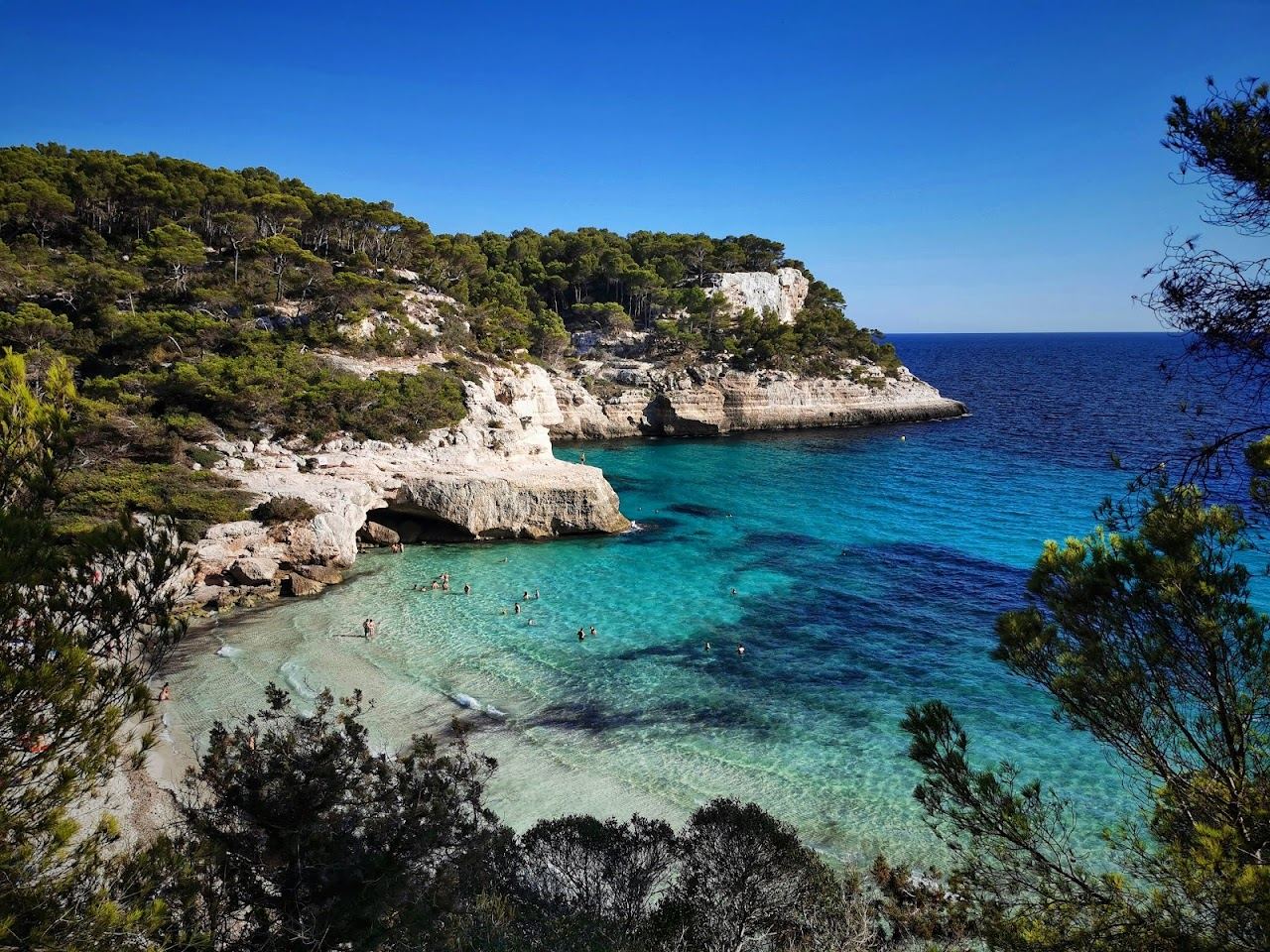 Pale sand, clear turquoise water and low limestone cliffs at Cala Mitjana in Menorca