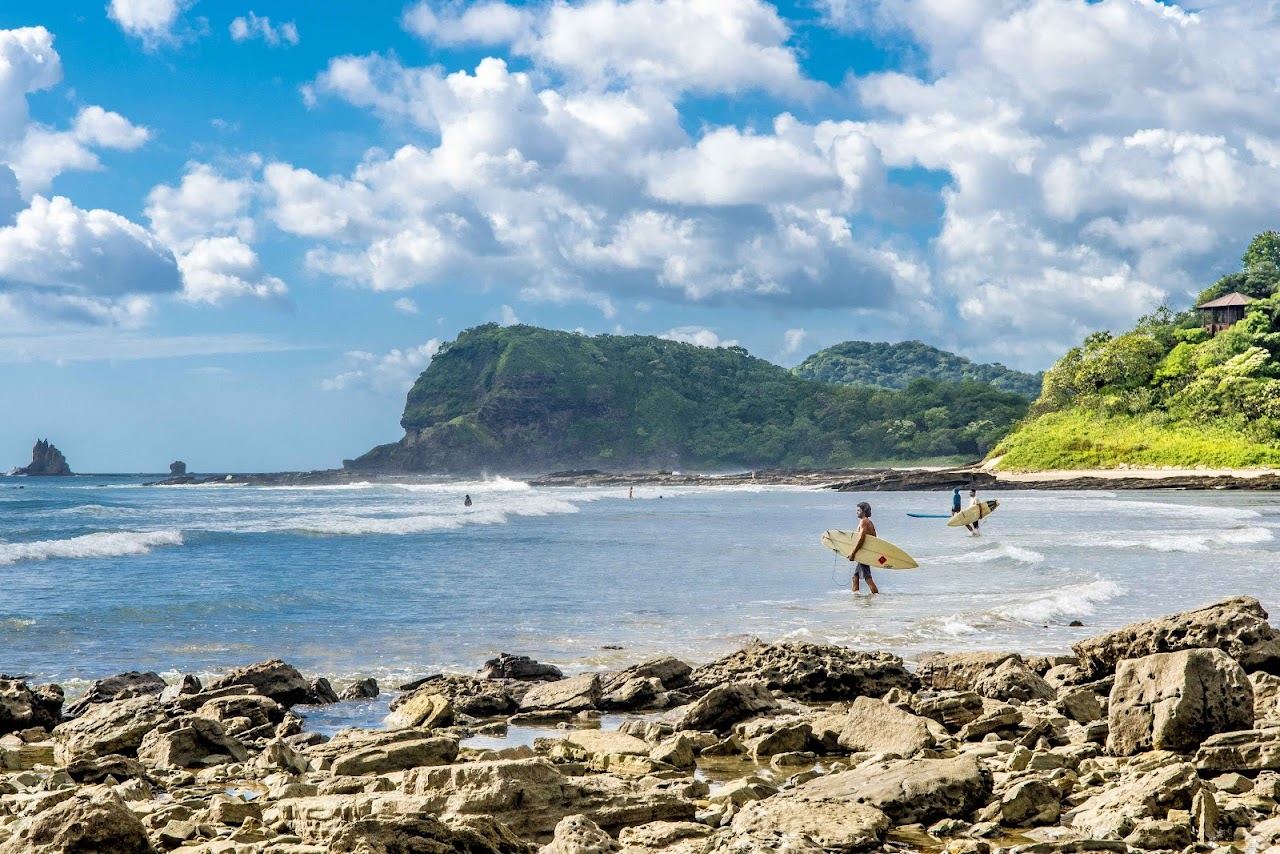 A horseshoe bay of golden sand and clean surf framed by green headlands at Playa Maderas, Nicaragua