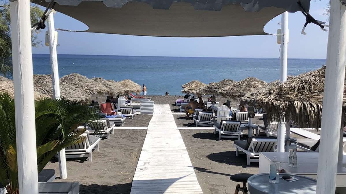 Wooden beach beds and triangular canopies on the black sand of Perivolos in front of Chilli Beach Bar, Santorini