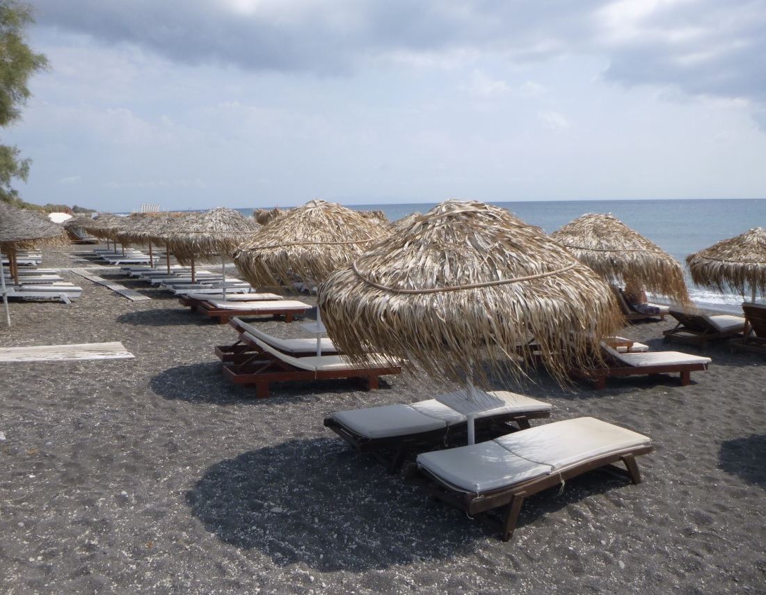 The long dark volcanic sand and open Aegean water of Perivolos beach on the southeast coast of Santorini