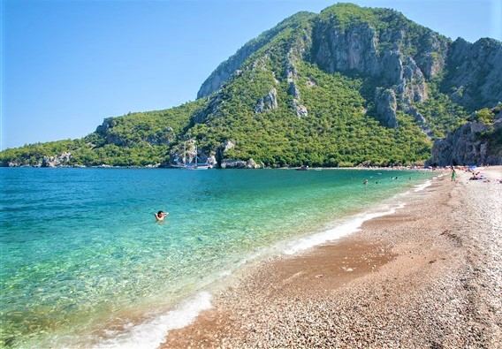 The long quiet pebble and coarse sand shore of Cirali beach near Antalya backed by green mountains