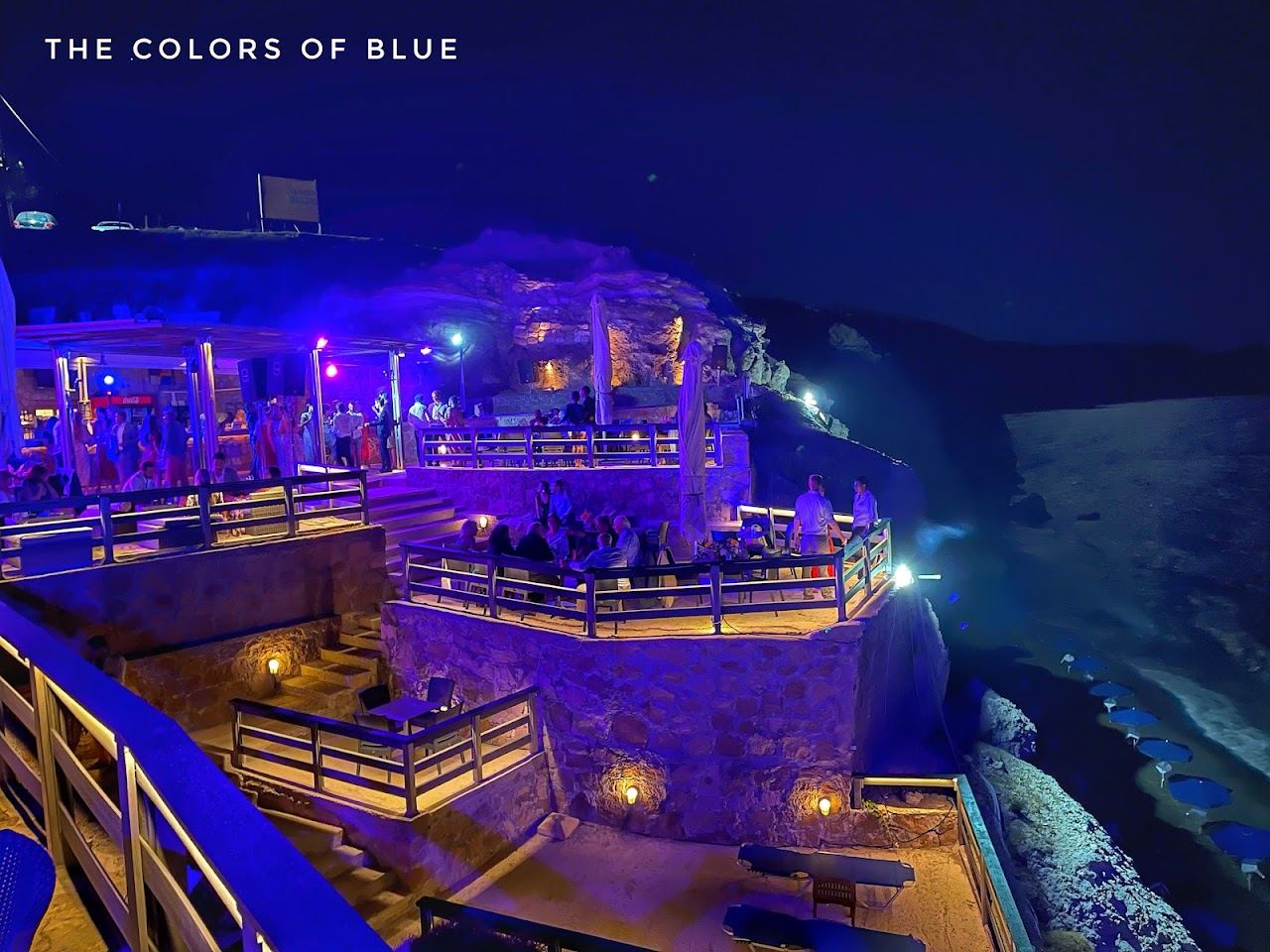 The terraces of Deep Blue beach bar stacked on the red rock above the water at Paliochori in Milos