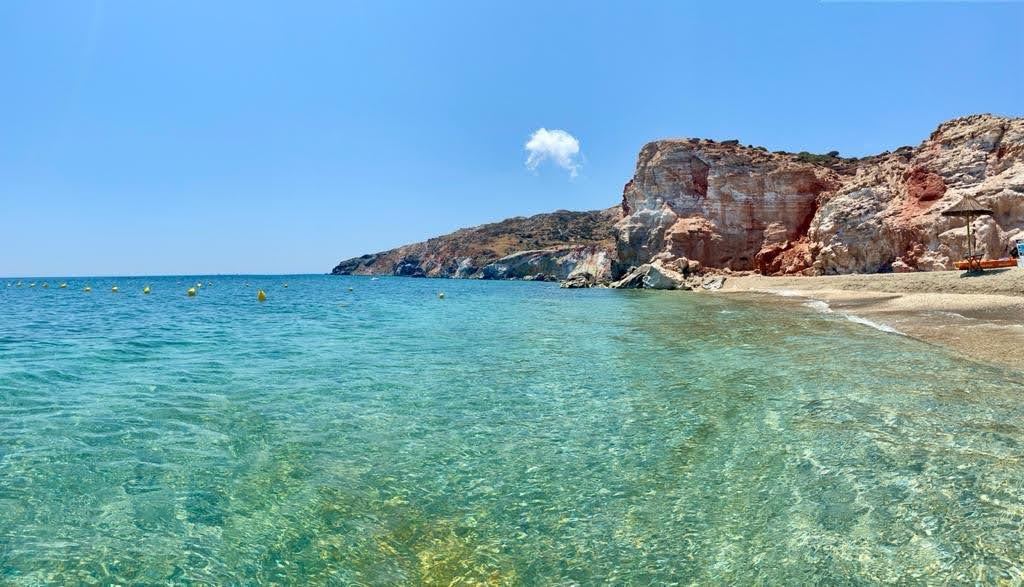Umbrellas and clear water along the volcanic sand of Paliochori beach seen from the shoreline in Milos
