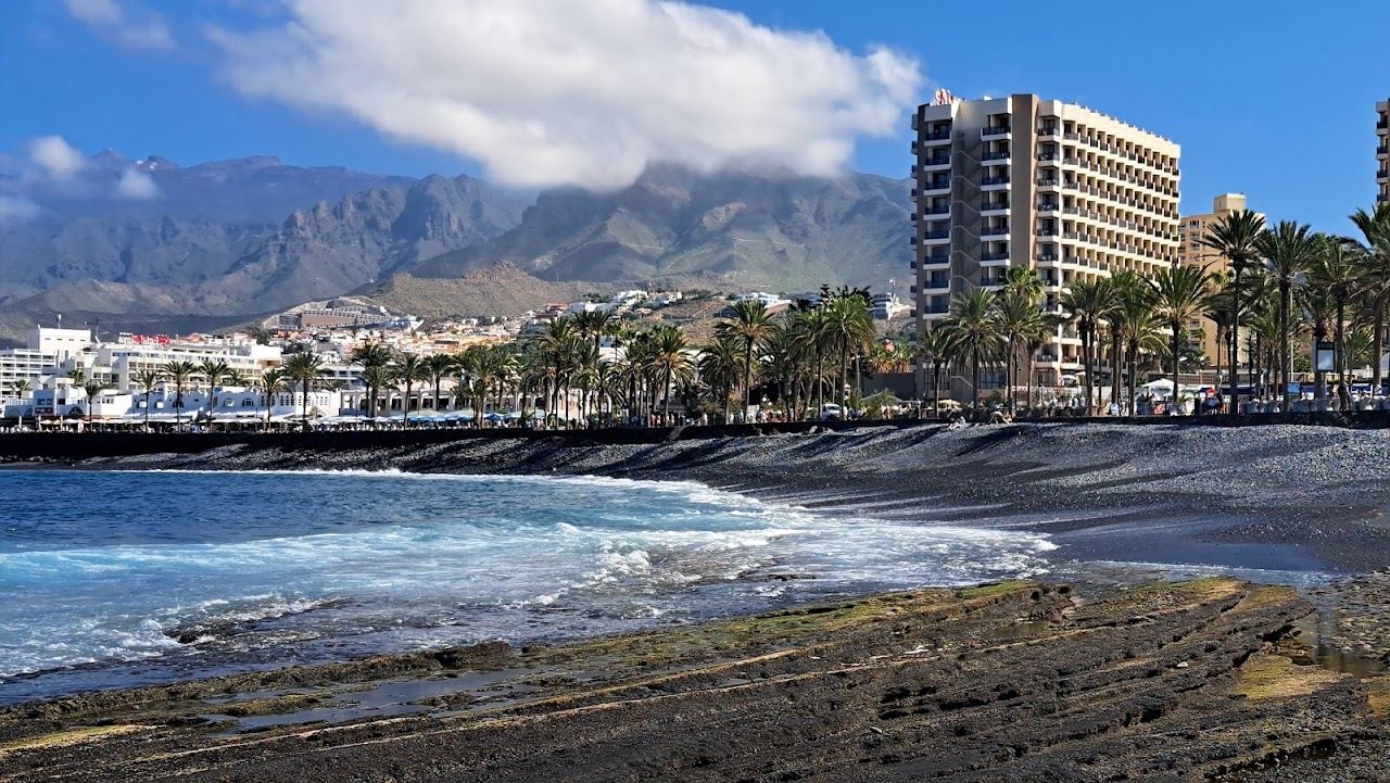 A sunny resort beach with a long promenade and cafes at Playa de las Americas in Tenerife