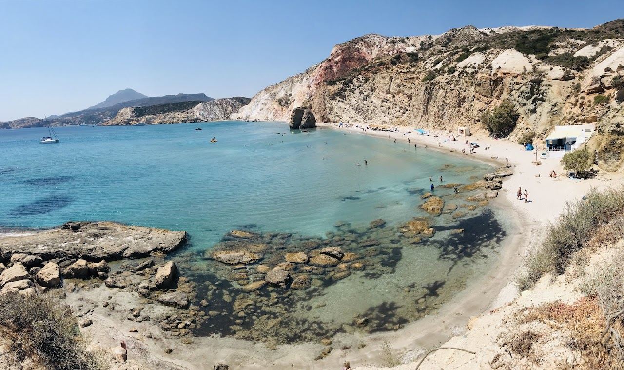 The long sweep of sand at Firiplaka below striped volcanic cliffs with calm clear water on the south coast of Milos