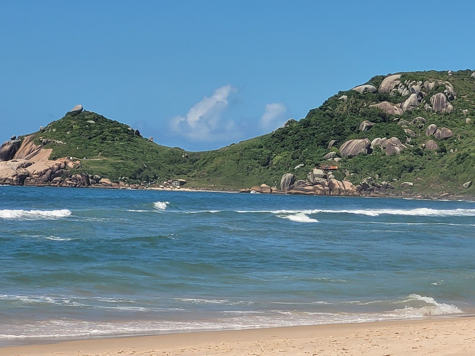 Green headlands framing the pale sand and blue surf of a scenic beach in Florianopolis Brazil