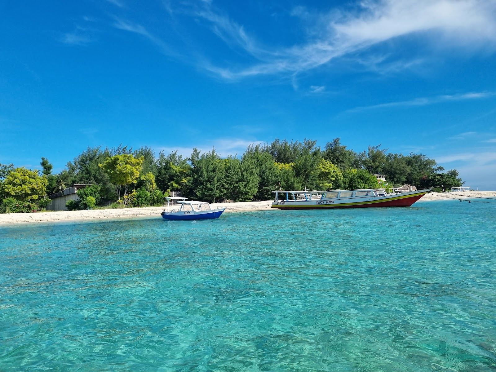 Clear shallow water and simple wooden boats off a car free beach in the Gili Islands