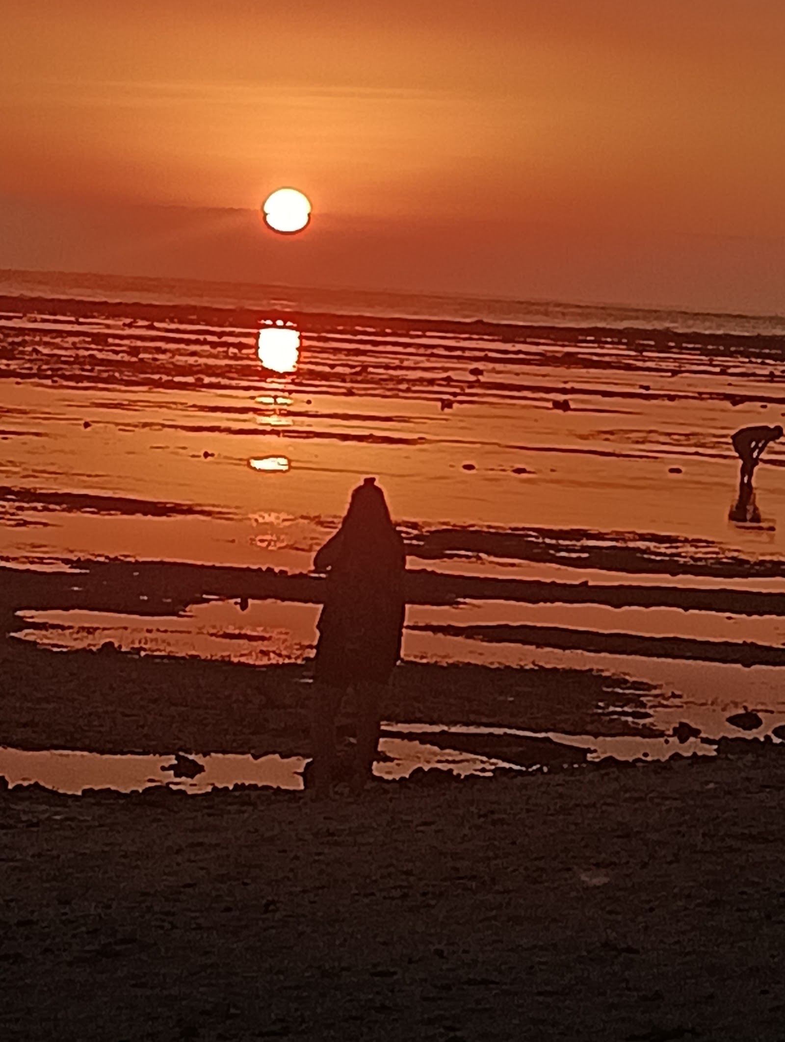 A swing standing in the shallows of Sunset Beach on Gili Trawangan with the sun low over the sea toward Bali