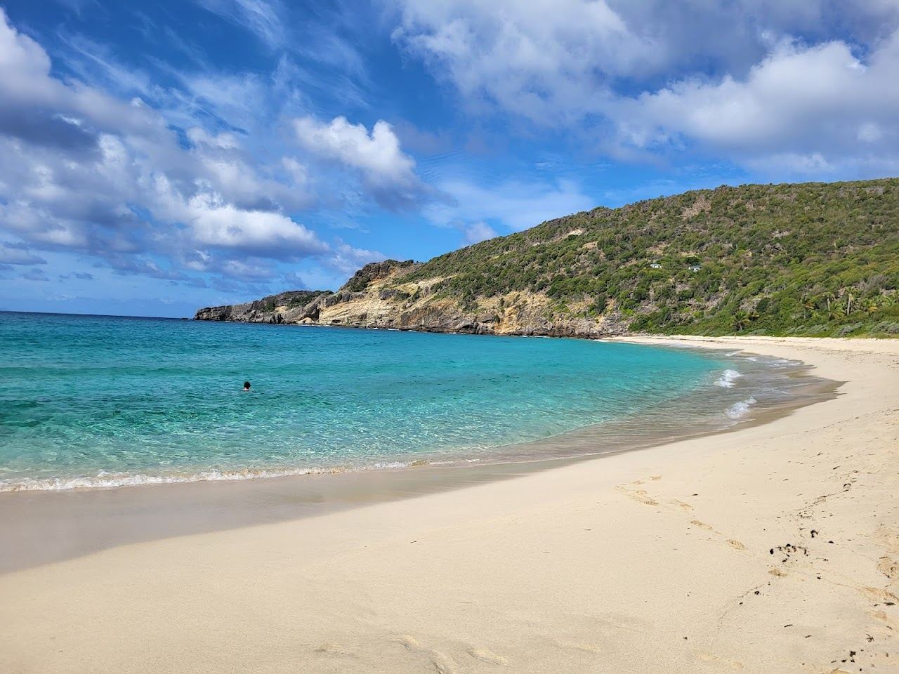 The wild white sand cove and clear water of Anse du Gouverneur wrapped by green hills on St Barths