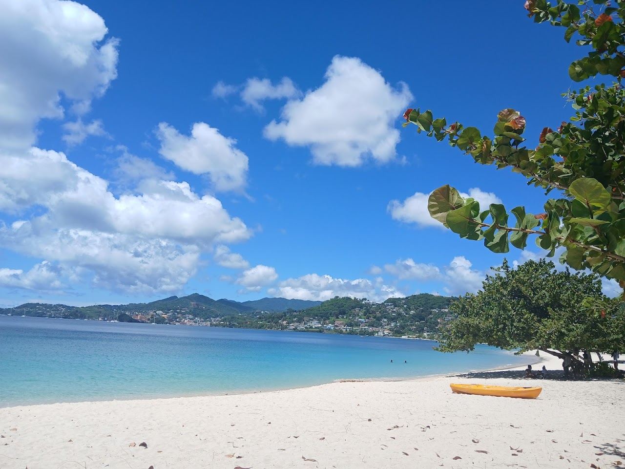 White sand and clear shallow water along Grand Anse Beach with green hills behind near St George's Grenada