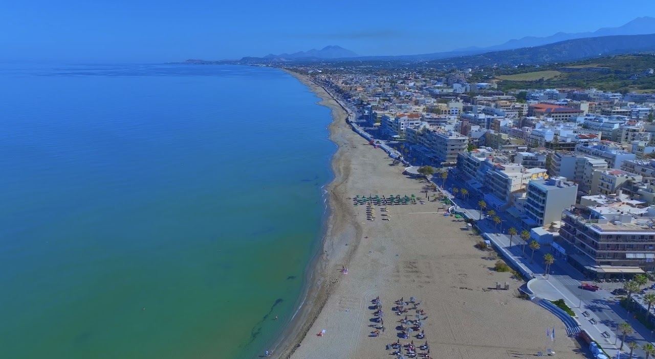 Long sandy town beach at Rethymno in Crete with umbrellas and calm water
