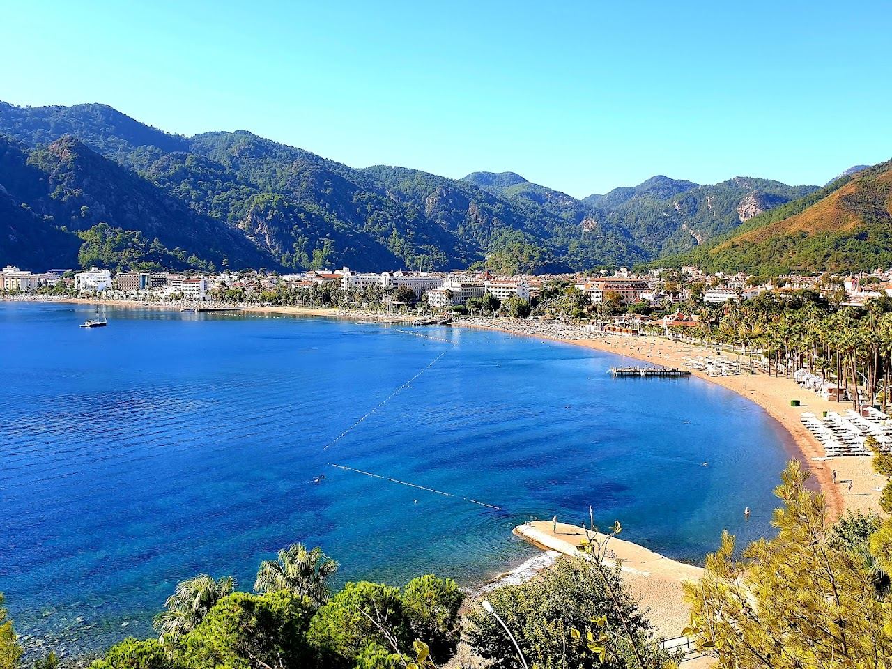 The sweep of Icmeler bay with calm water and wooded hills behind the beach
