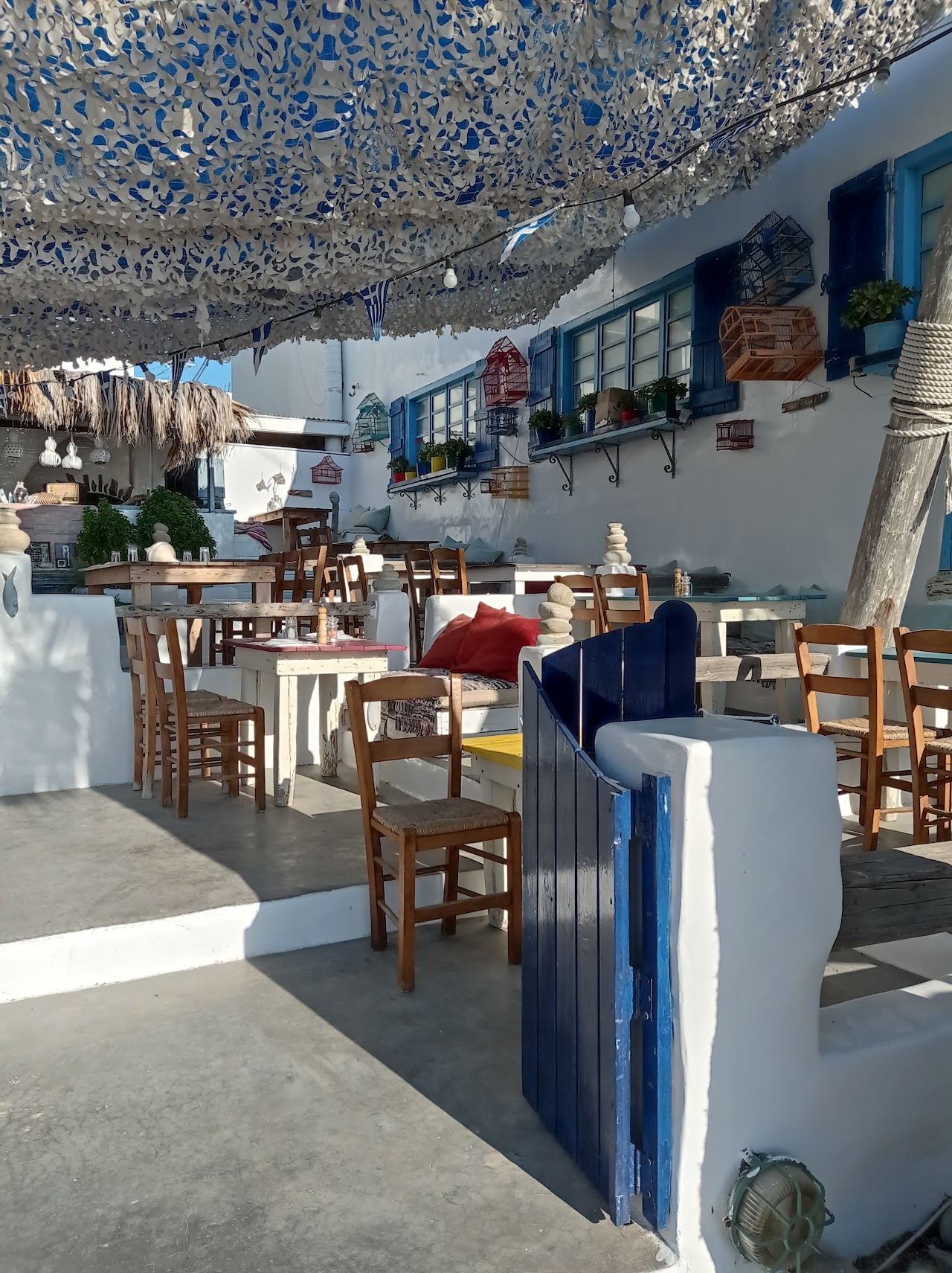 Whitewashed seafront terrace of Island Bar at Agia Anna in Naxos with blue shutters and shaded tables