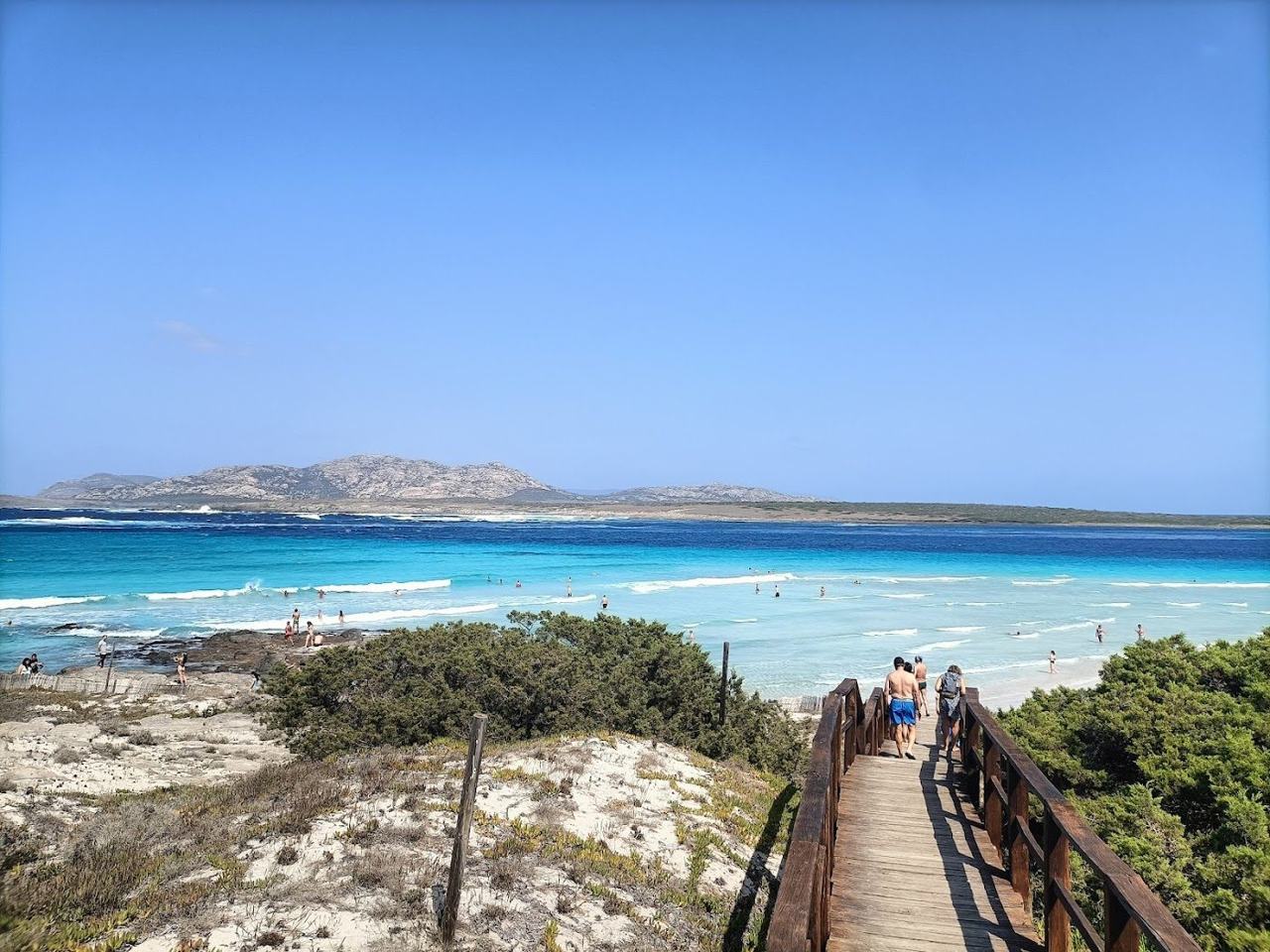 Pale sand and bright turquoise shallows on a Sardinian beach under clear June skies