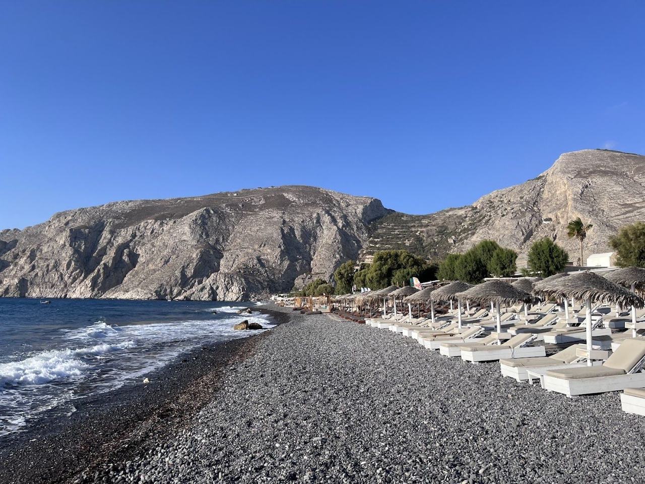 The promenade and dark pebble shore of Kamari Beach under the Mesa Vouno cliff on Santorini