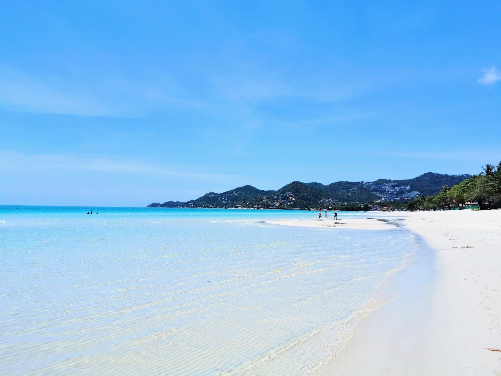 Soft white sand and clear shallow water along the long curve of Chaweng Beach on Koh Samui