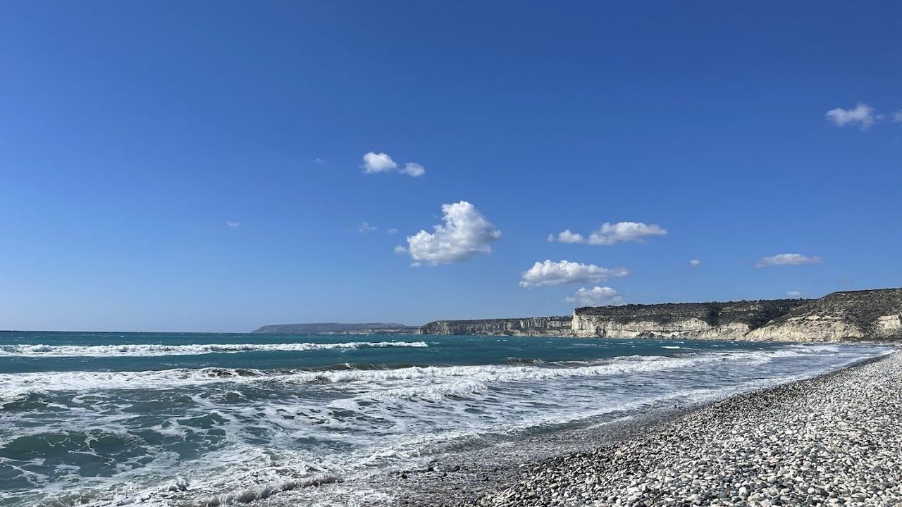 Long open beach of sand and shingle below low cliffs with breaking waves at Kourion near Limassol in Cyprus