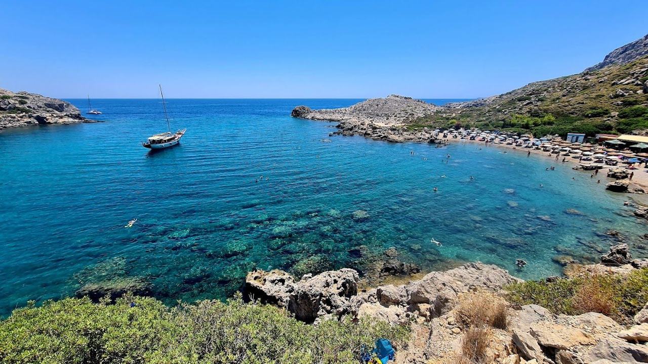 Clear calm water and a sheltered sand and pebble shore at Ladiko cove on the headland near Faliraki in Rhodes