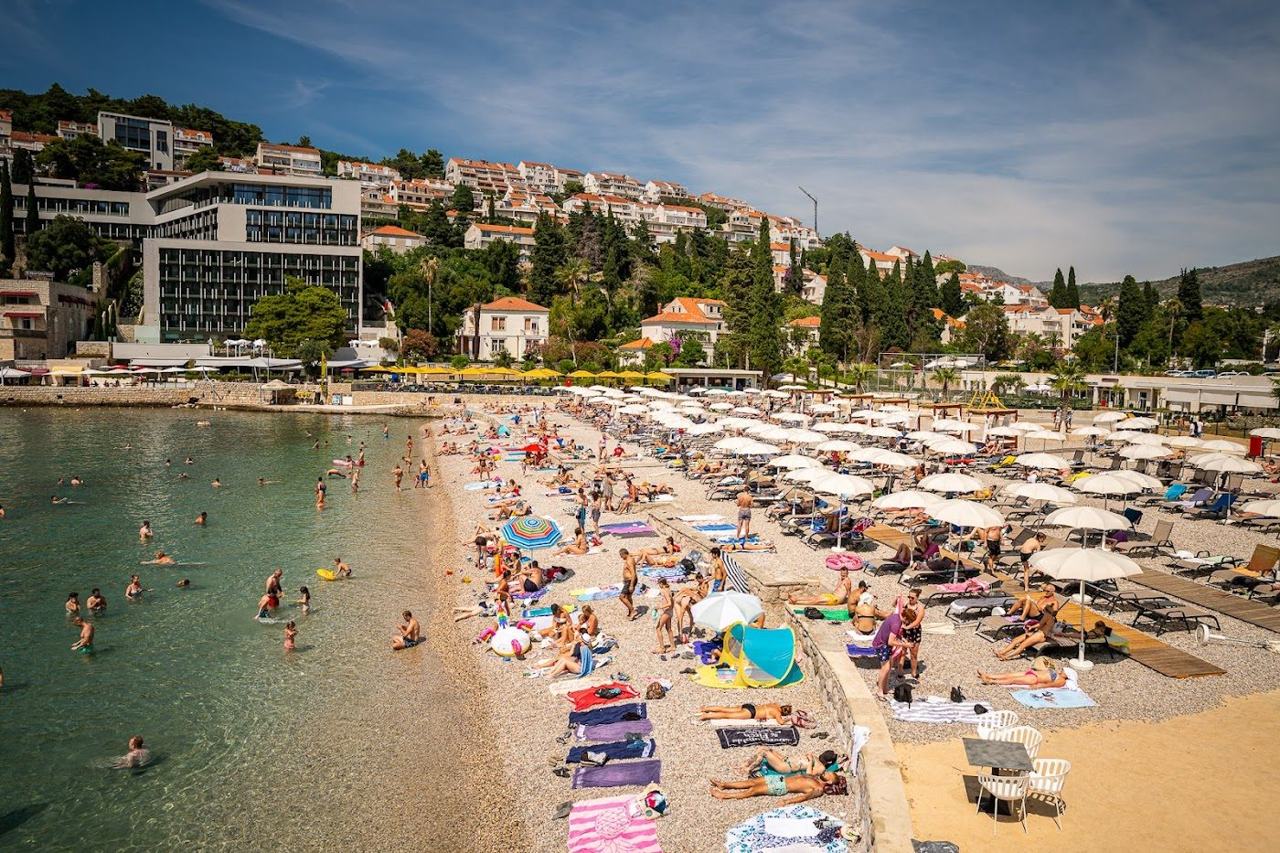 Lapad Beach in Uvala Lapad bay at Dubrovnik with pebble shore, calm water and the pedestrian promenade of bars behind on the Dalmatian Coast