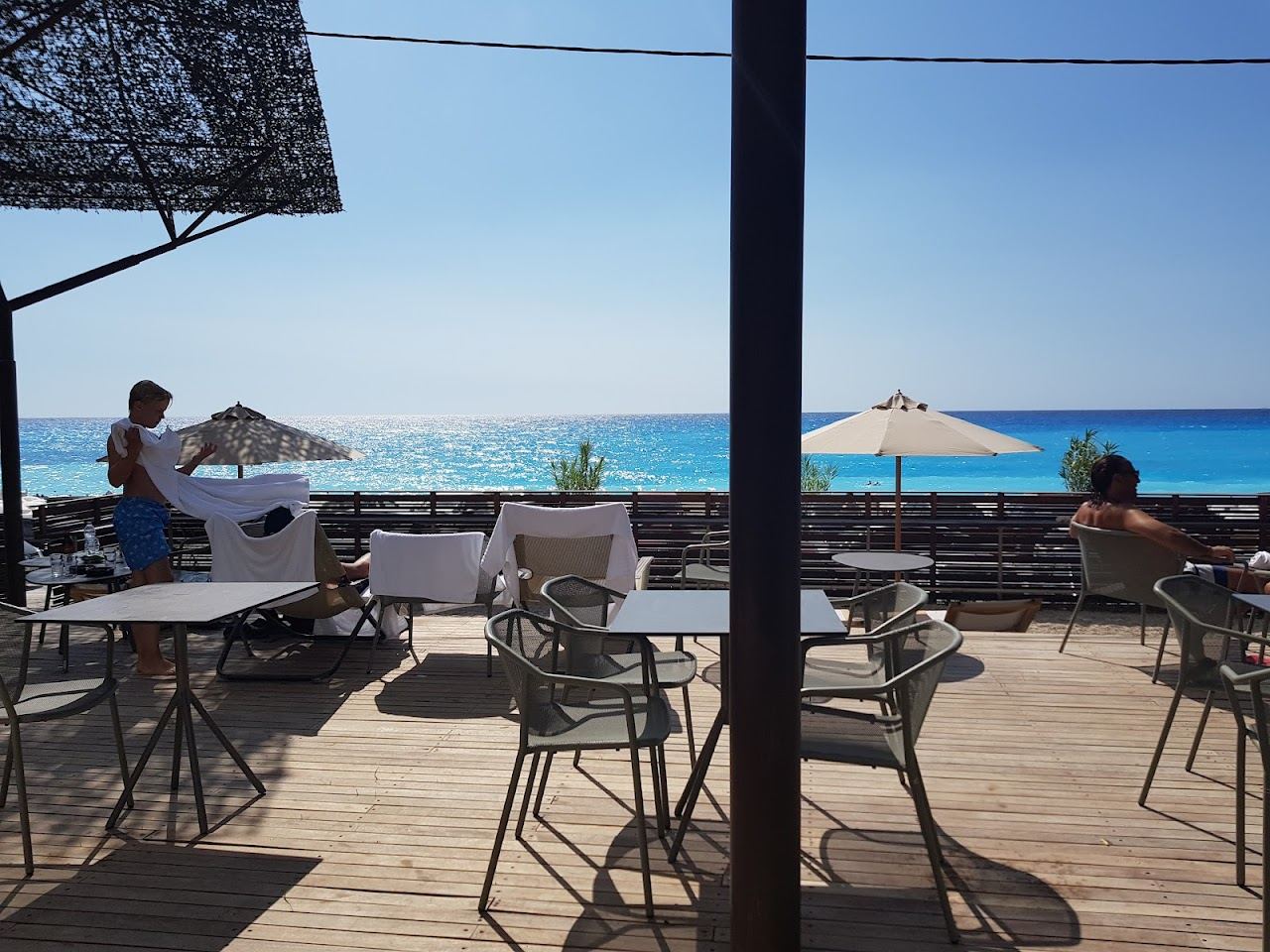 A lively west coast Lefkada beach with bars and loungers above pale sand and clear water