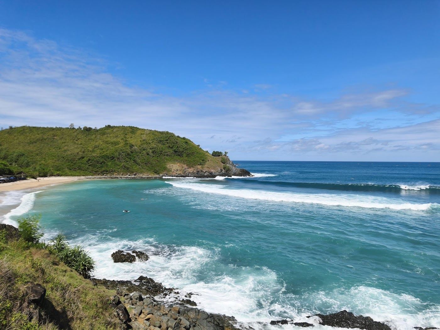 Pale surf cove framed by green headlands with waves rolling in at Mawi on the south coast of Lombok