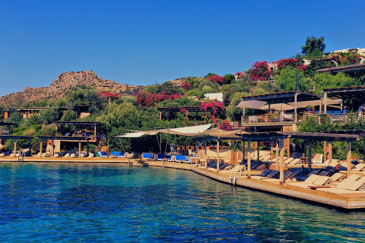 Sunbeds and white parasols on the timber beach deck of Macakizi over the water at Turkbuku, Bodrum