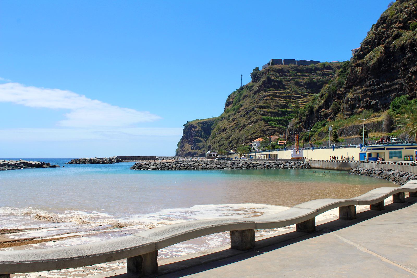 Sheltered golden sand and still turquoise water held behind the marina breakwater at Calheta on the south coast of Madeira