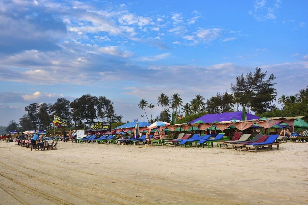 Mandrem Beach wide soft pale sand with calm shallow water and palms in North Goa